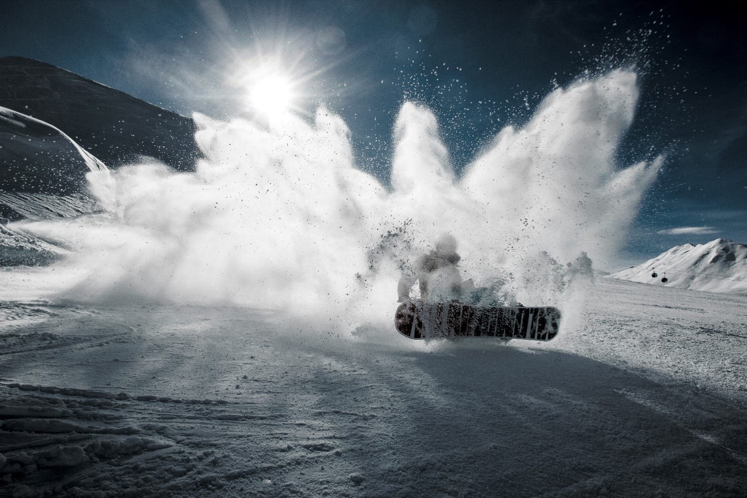 A snowboarder carving through deep powder, throwing a wall of snow into the sun